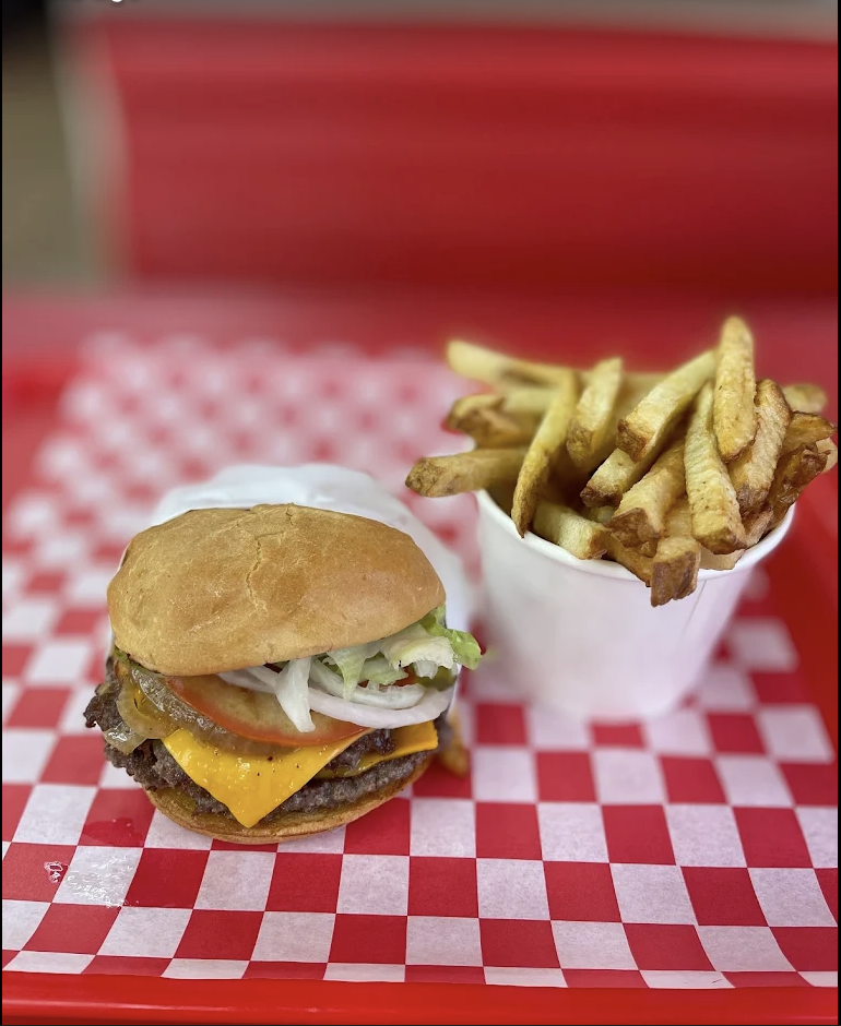 A smash burger and fries on a red checkered tray in a red diner booth.