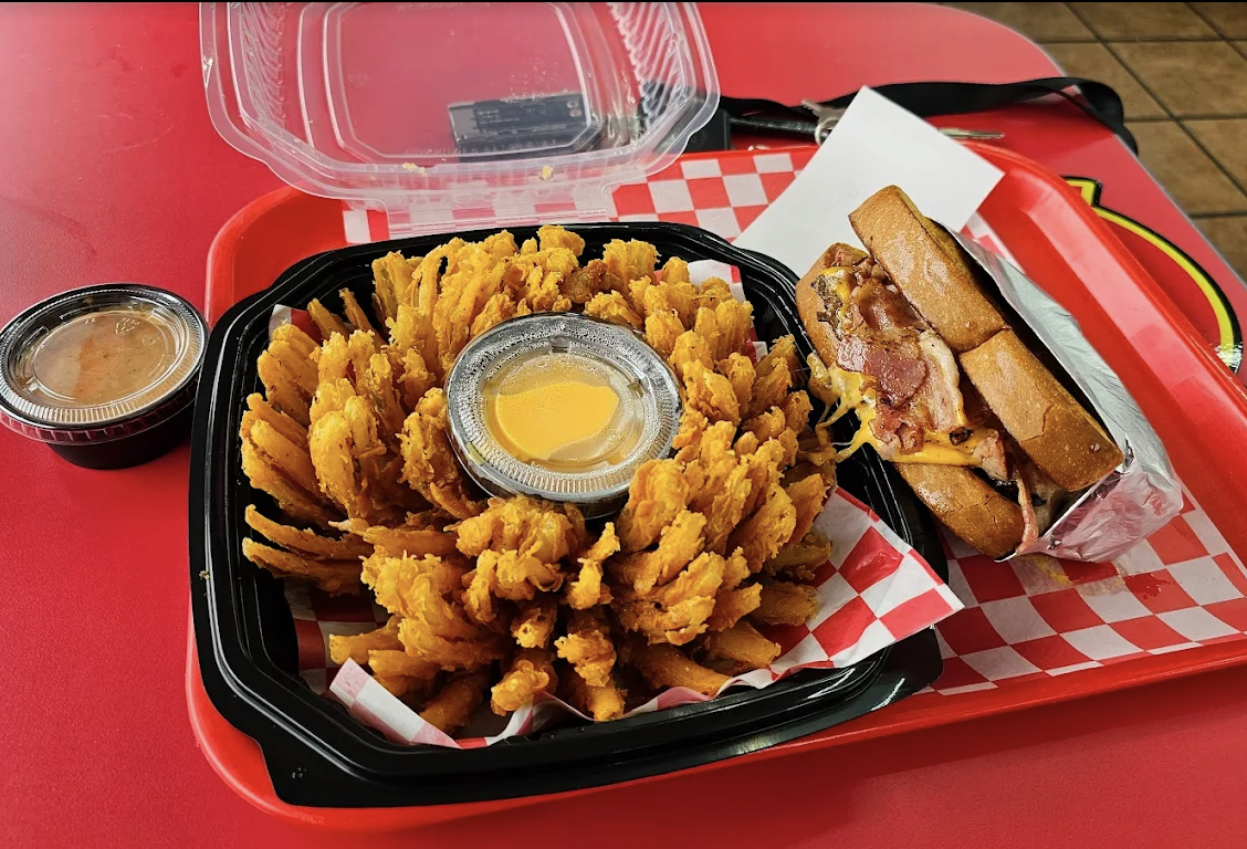 The Best Bomb Classic blooming-onion-style appetizer in a black container with dipping sauce on a red tray.