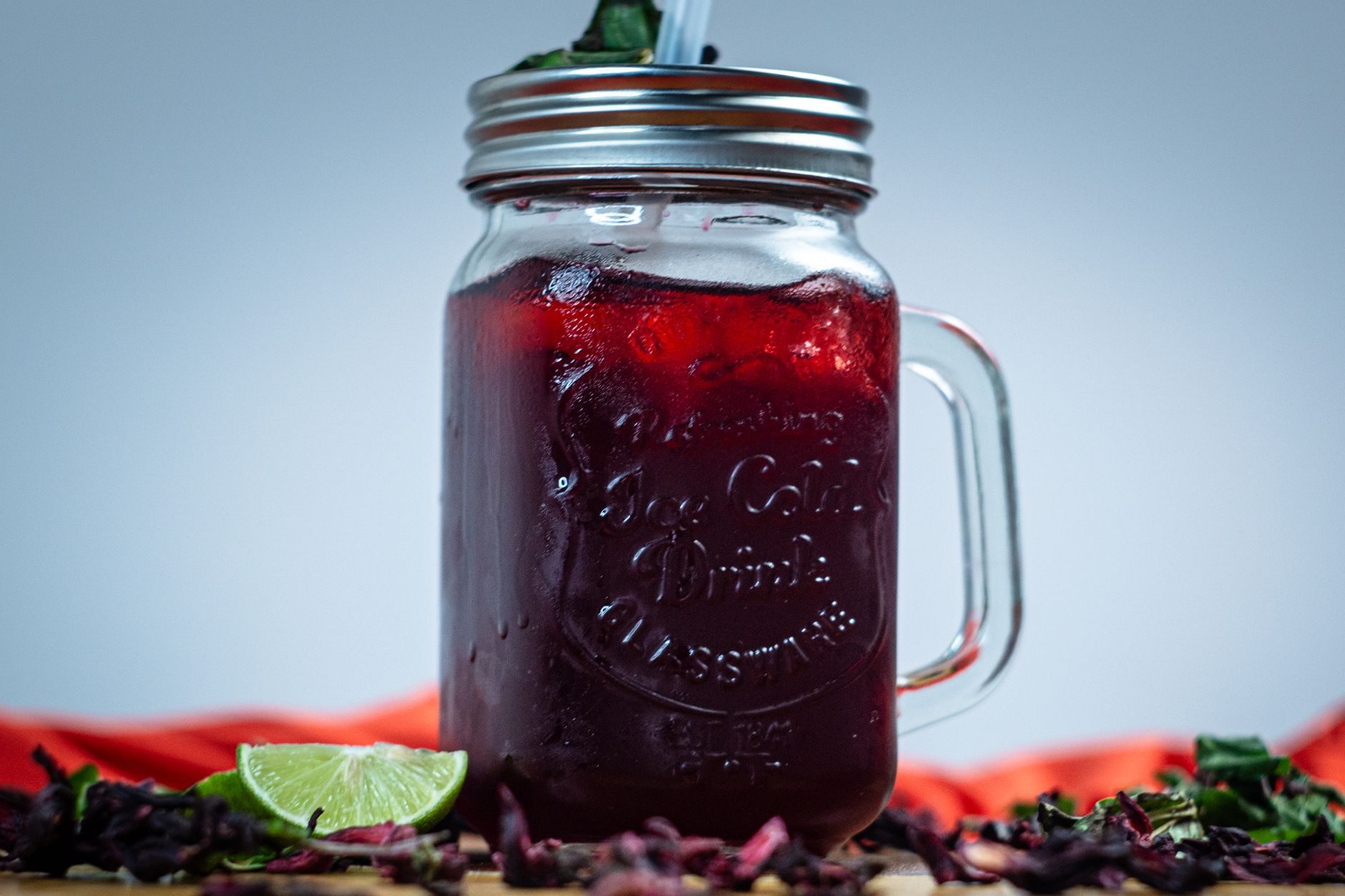 A deep ruby-red hibiscus agua de jamaica in a mason jar with lime and mint.