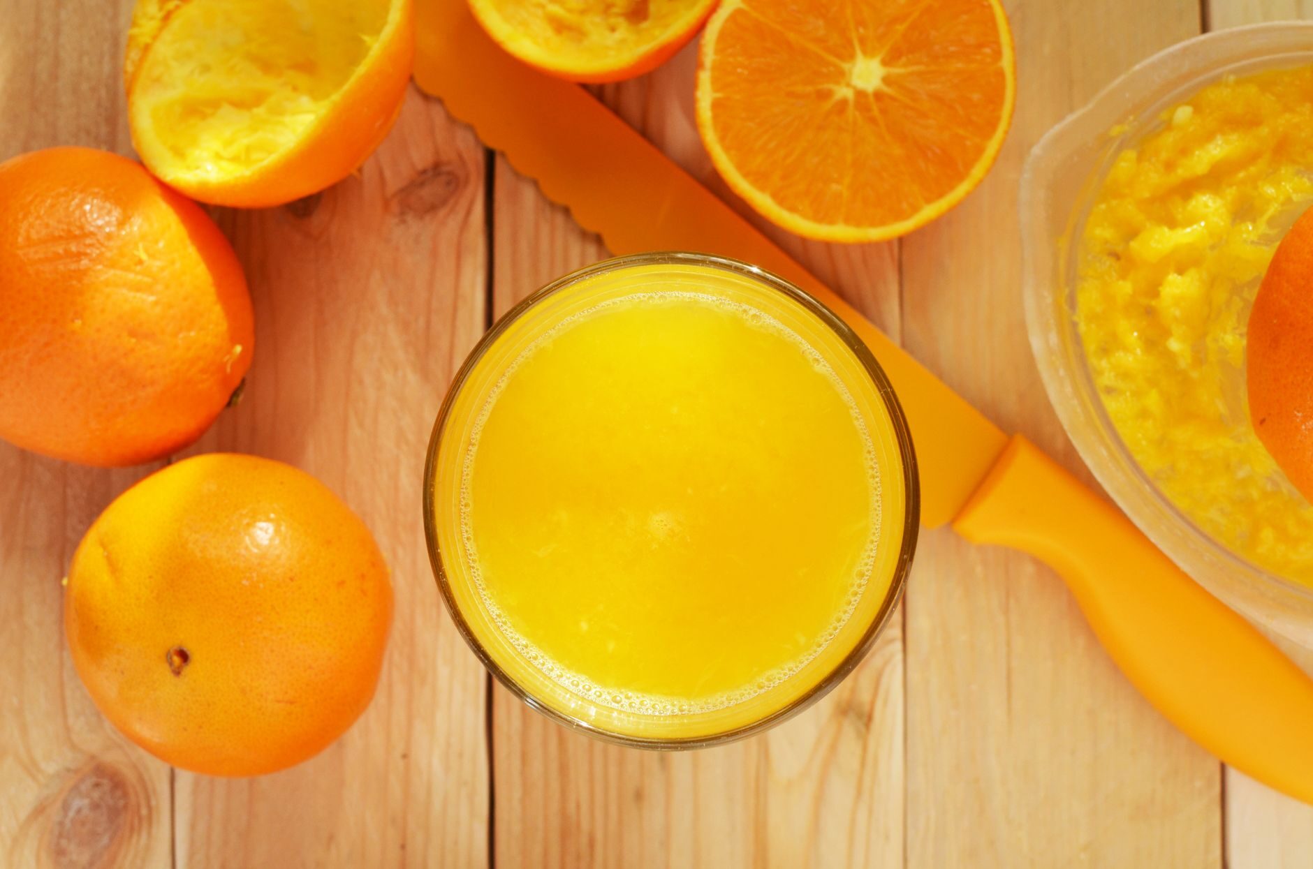 A bright glass of fresh orange juice surrounded by whole and halved oranges on a wooden board.