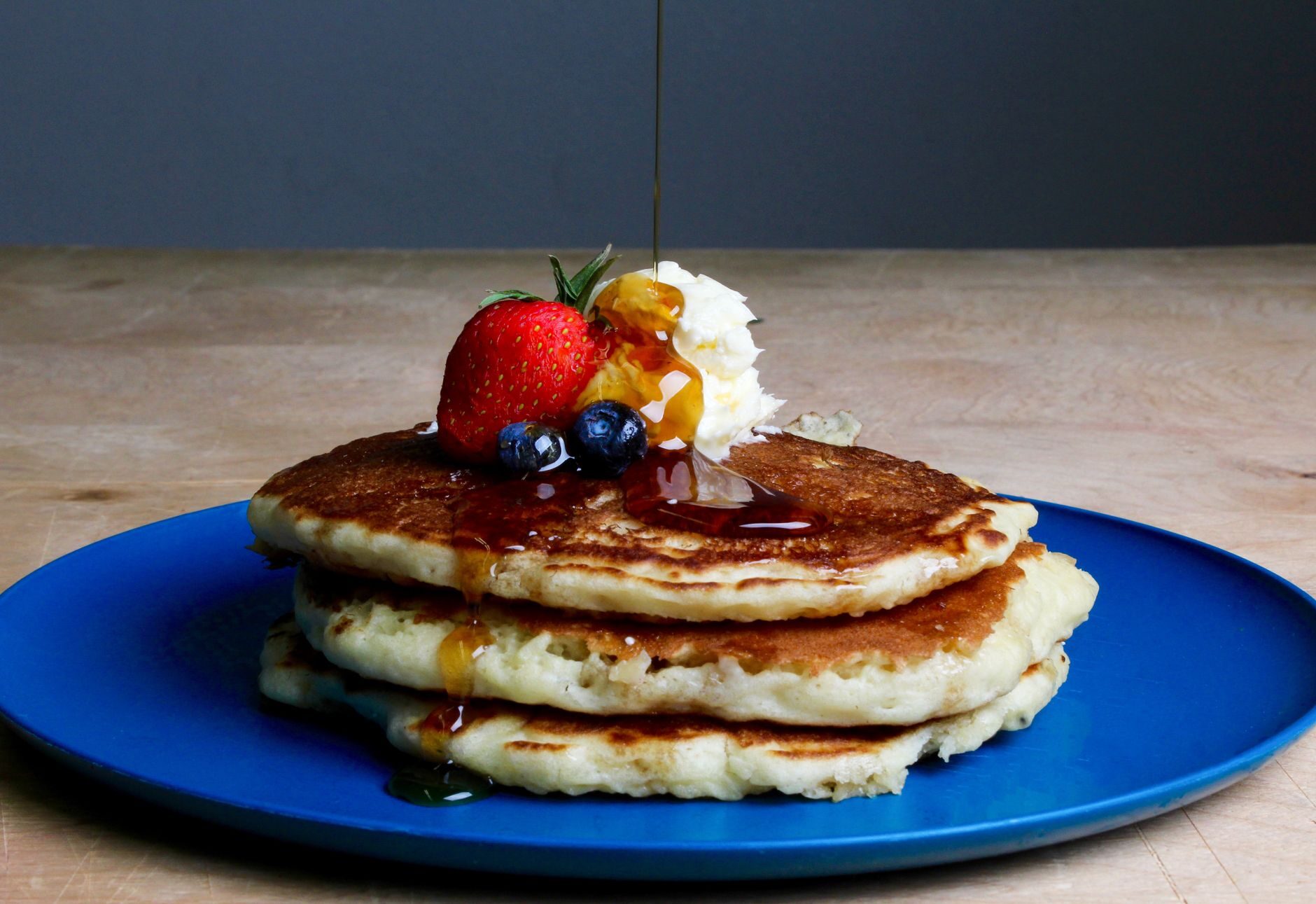 A diner stack of pancakes with berries, whipped cream, and syrup.
