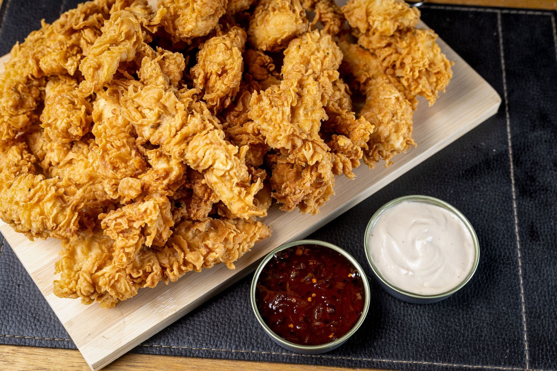 A generous platter of golden crispy chicken tenders with ranch and barbecue dipping sauces.